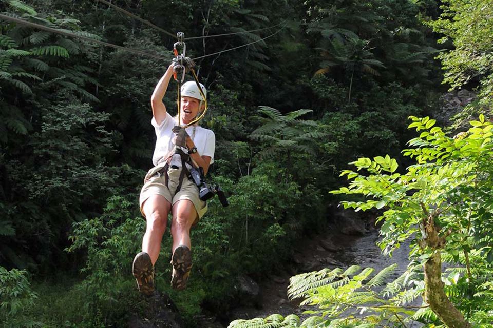 A person zip-lining through dense green forest.