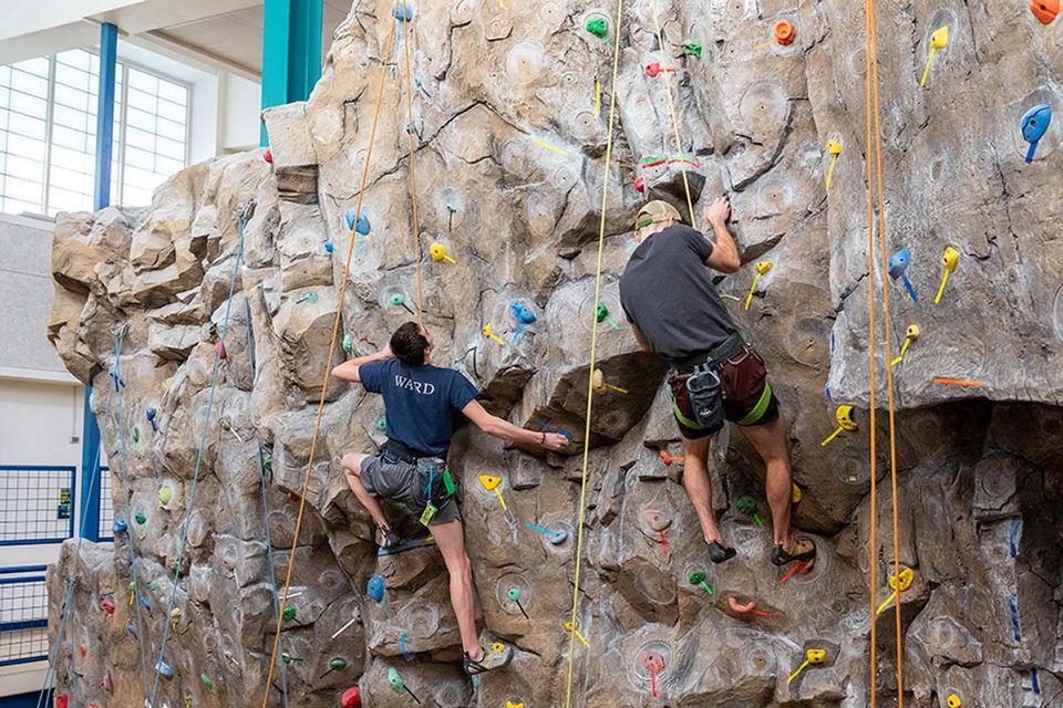 Two climbers scaling the climbing wall at the WVU Student Rec Center.