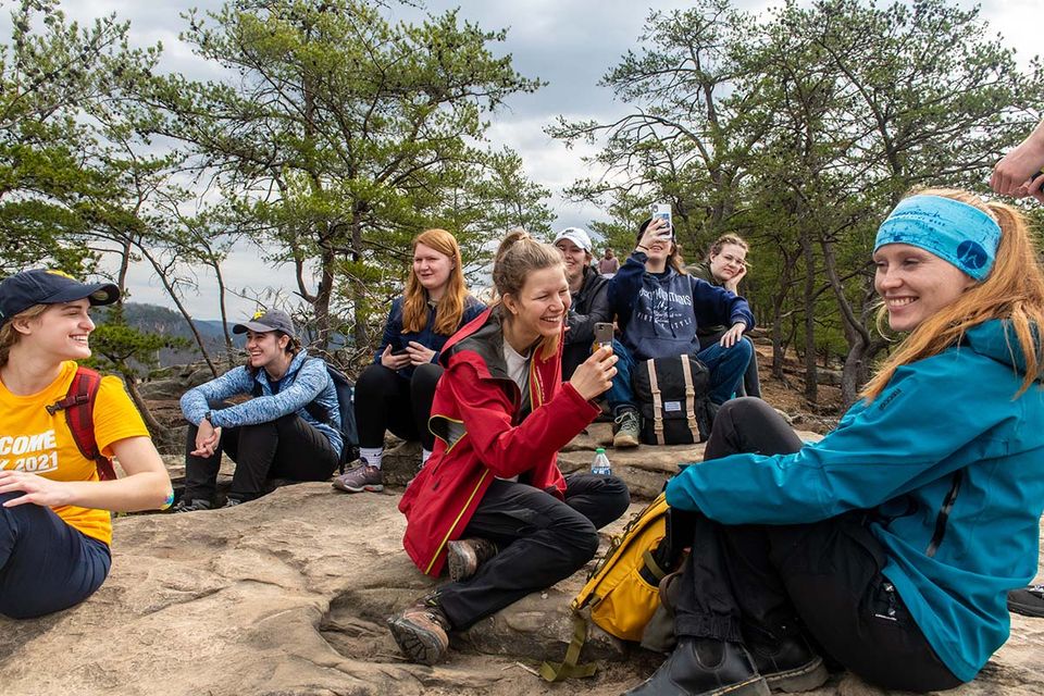 A group of students sitting on a rock while taking a rest from their hiking trip.