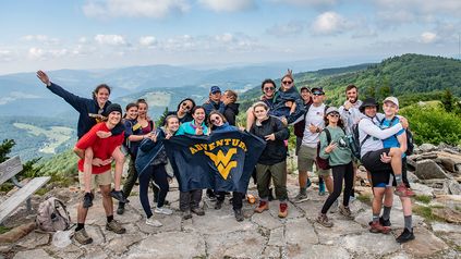 Adventure Quest participants taking a group photo on a cliff with the Adventure WV Flag