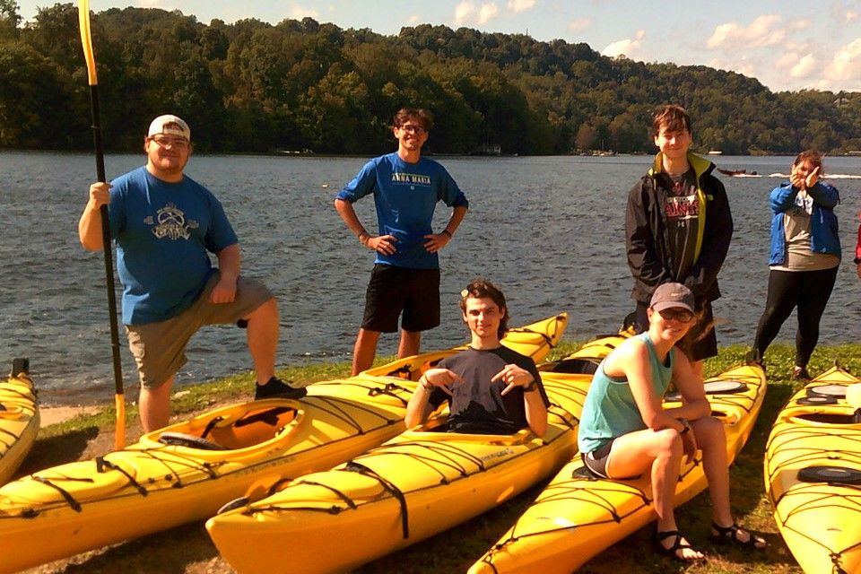 Group of students posed on and around kayaks while on the shore of Cheat Lake