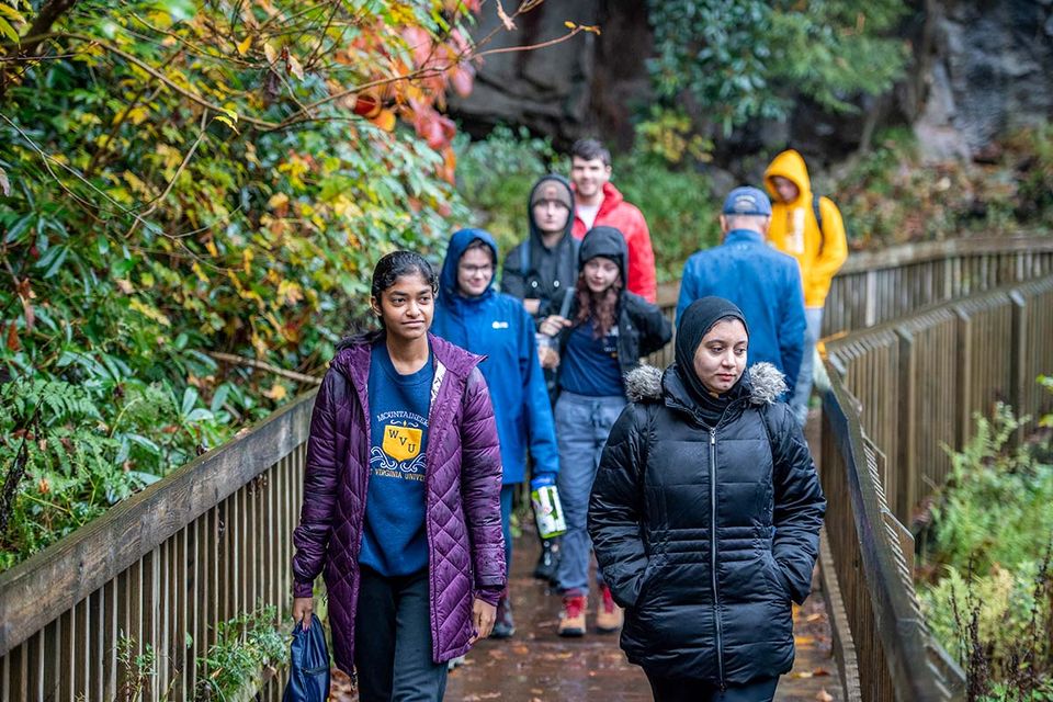 People walking across a rainy wooden bridge in the forest of Black Water Falls.
