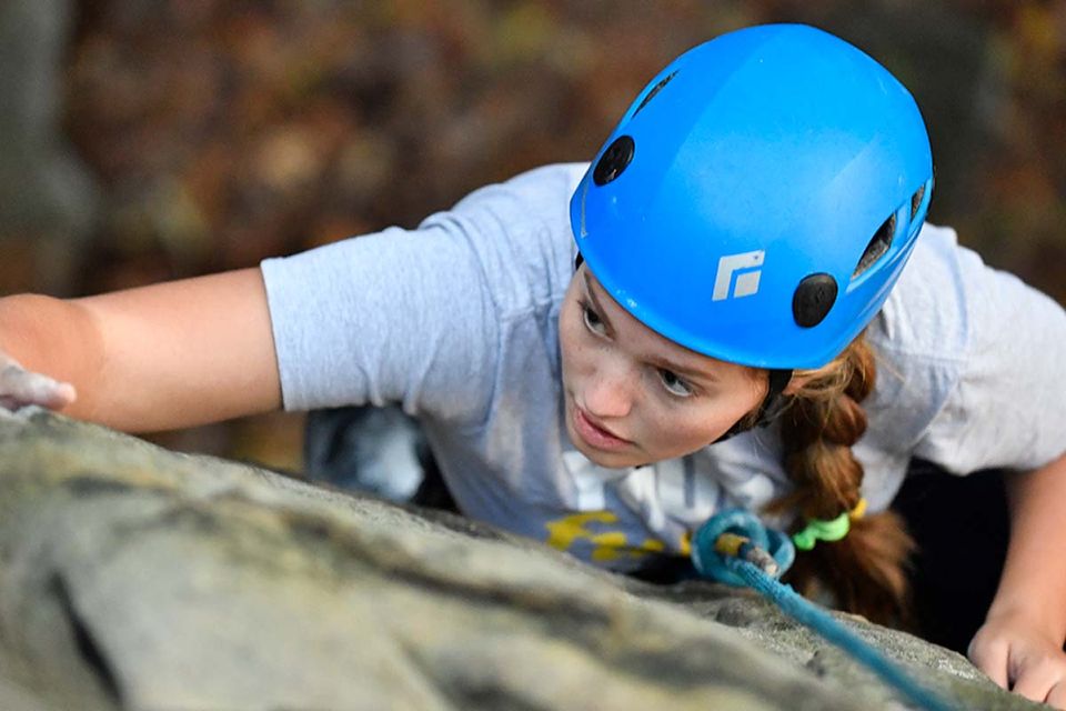 View from above of a climber scaling a rock in a light blue helmet.